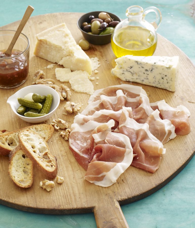 The classic charcuterie board with slices of Prosciutto di Parma, crostini, assorted cheeses, cured olives, petite pickles, olive oil and jam