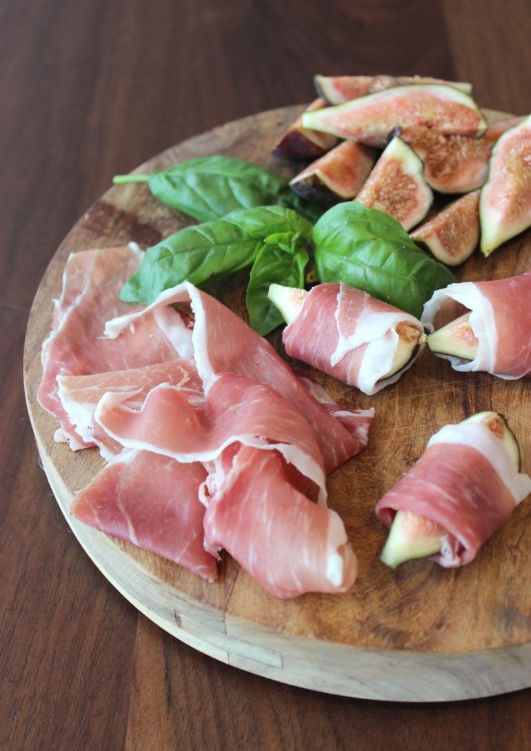 Sweet figs wrapped in slices of prosciutto displayed on a charcuterie board