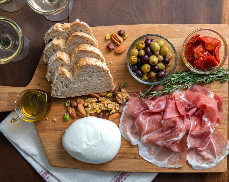 The classic charcuterie board with slices of Prosciutto di Parma, roasted red pepper, assorted nuts, burrata cheese, cured olives, and olive oil